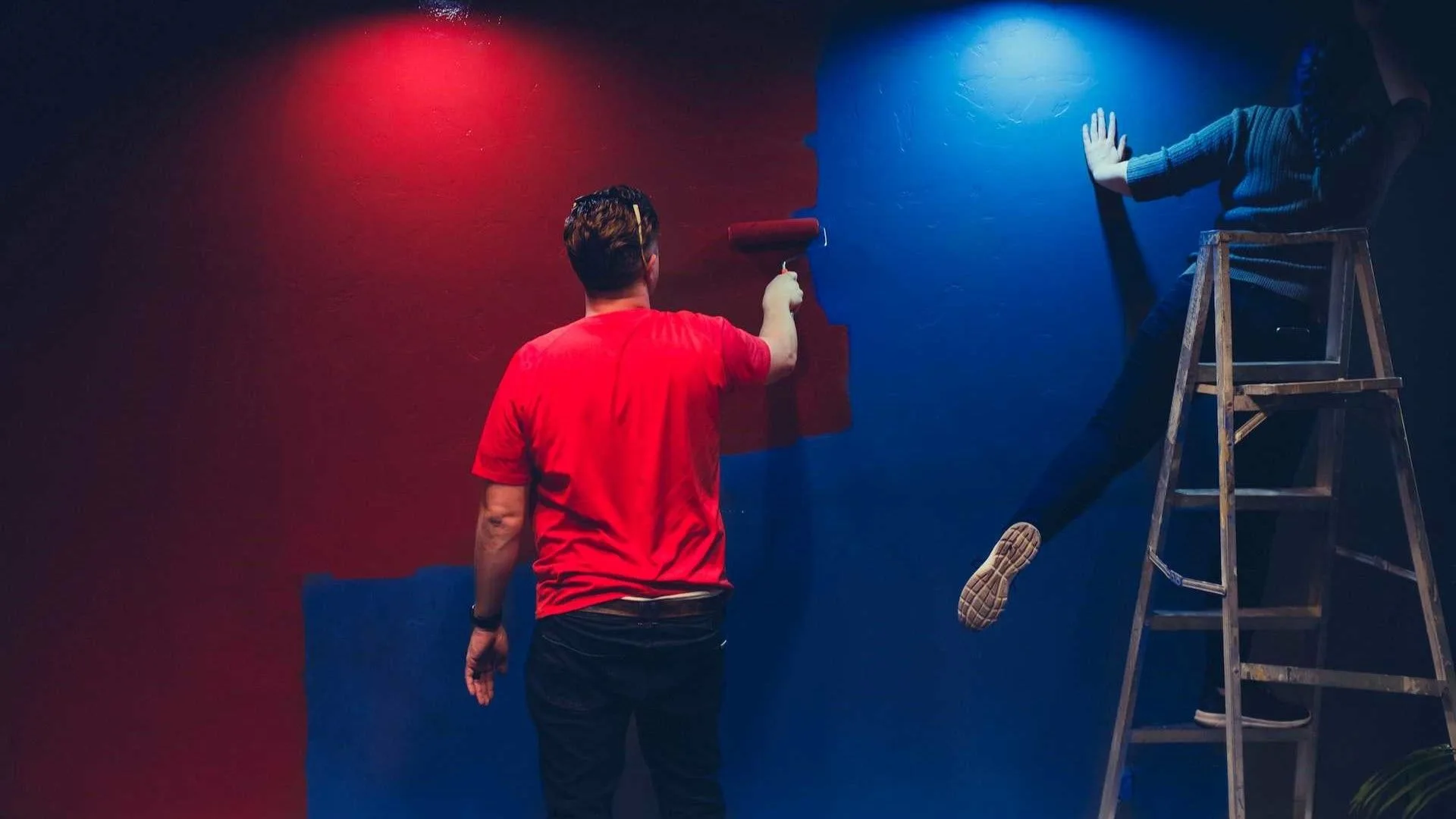 Twee mensen verven de muur met rollers in de kleur rood en blauw